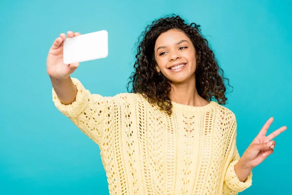 Mulher americana africana alegre tomando selfie no smartphone enquanto mostra sinal de paz isolado no azul — Fotografia de Stock