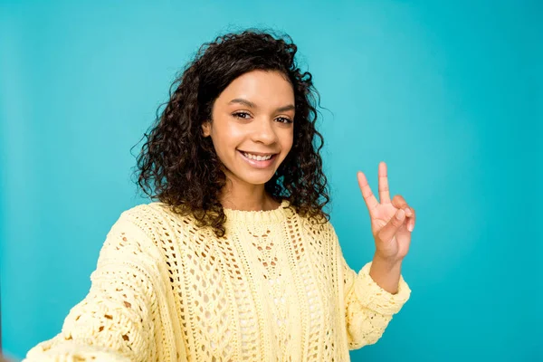 Alegre afro-americana mulher tomando selfie e mostrando sinal de paz isolado no azul — Fotografia de Stock