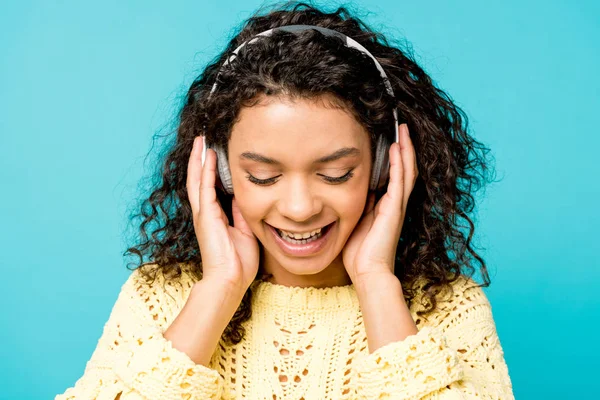 Atraente encaracolado menina americana africana ouvir música em fones de ouvido com olhos fechados isolado em azul — Fotografia de Stock