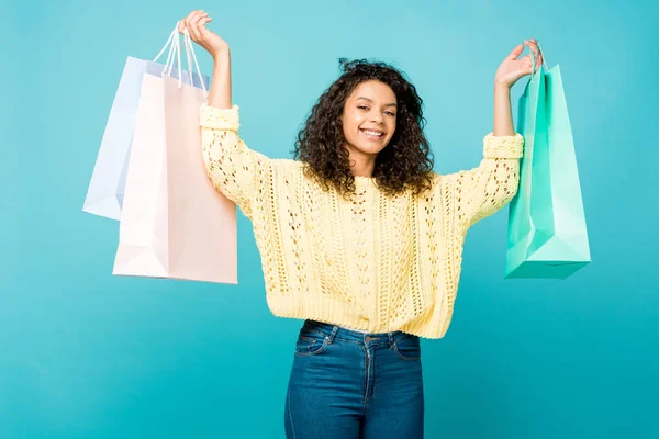 Happy african american girl holding shopping bags while standing isolated on blue — Stock Photo