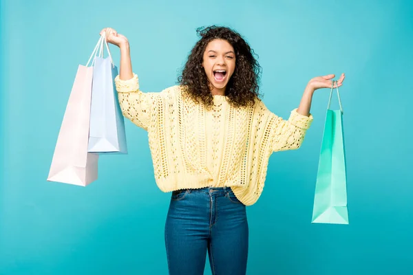 Impactado chica afroamericana sosteniendo bolsas de compras y gritando mientras estaba de pie en azul - foto de stock