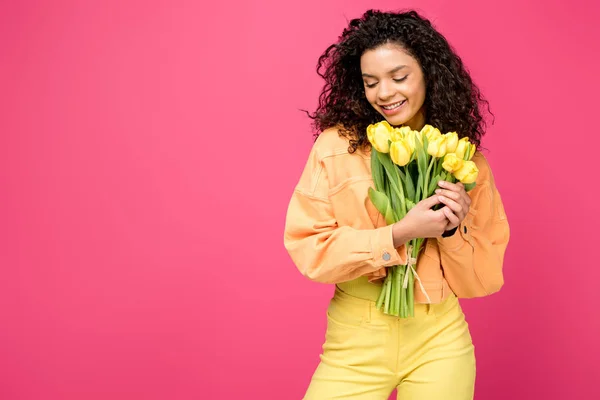 Sonriente afroamericano chica sosteniendo amarillo tulipanes aislado en carmesí - foto de stock
