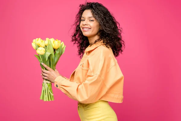 Mujer afroamericana feliz sosteniendo tulipanes amarillos aislados en carmesí - foto de stock