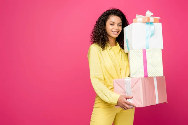 Belle femme afro-américaine frisée tenant des boîtes-cadeaux isolées sur cramoisi — Photo de stock