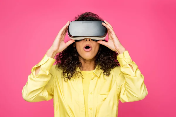 Schockiert lockige Afroamerikanerin trägt Virtual-Reality-Headset und zeigt mit den Fingern isoliert auf purpurrot — Stockfoto