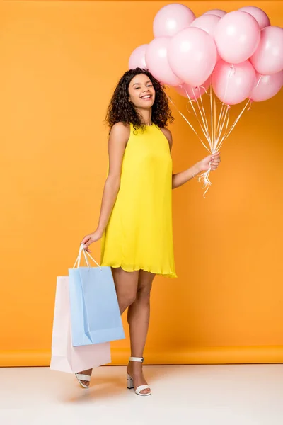 Happy african american woman holding shopping bags and pink air balloons on orange — Stock Photo