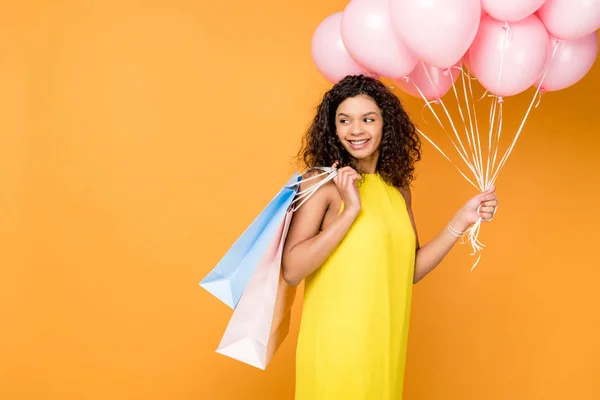 Happy african american woman holding shopping bags and pink air balloons isolated on orange — Stock Photo