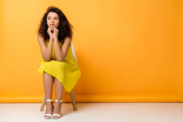Upset curly african american woman in yellow dress sitting on orange — Stock Photo