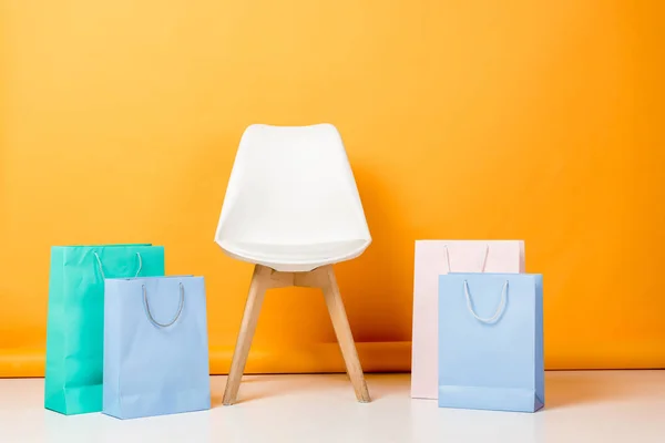 Stuhl in der Nähe von blauen, weißen und türkisfarbenen Einkaufstaschen auf orange — Stockfoto