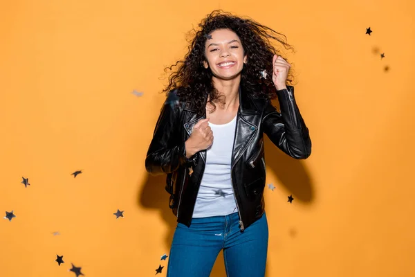 Beautiful curly african american girl standing near shiny confetti stars on orange — Stock Photo