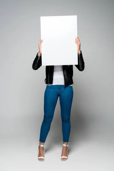 Africano americano jovem mulher cobrindo rosto com cartaz em branco, enquanto em pé sobre cinza — Fotografia de Stock