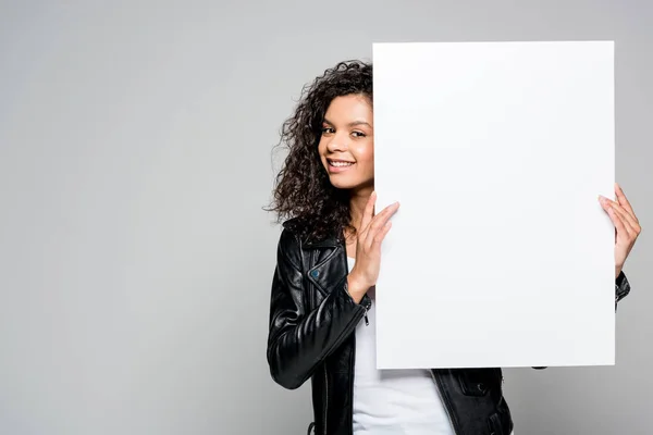 Smiling pretty african american young woman holding blank placard isolated on grey — Stock Photo