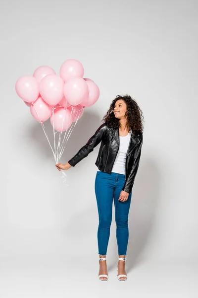 Happy african american young woman holding pink air balloons on grey — Stock Photo