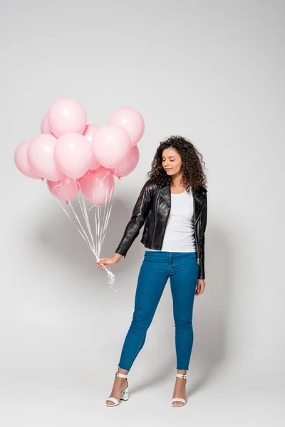 Beautiful african american young woman holding pink air balloons on grey — Stock Photo