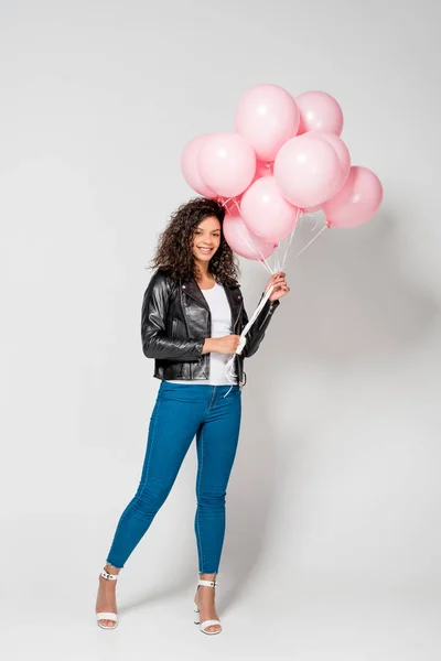 Smiling african american young woman holding pink air balloons on grey — Stock Photo