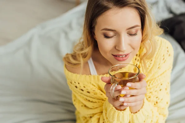 Hermosa mujer joven con los ojos cerrados sosteniendo taza de té en casa - foto de stock
