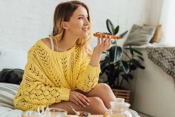 Beautiful girl in knitted sweater holding toast during breakfast at home — Stock Photo