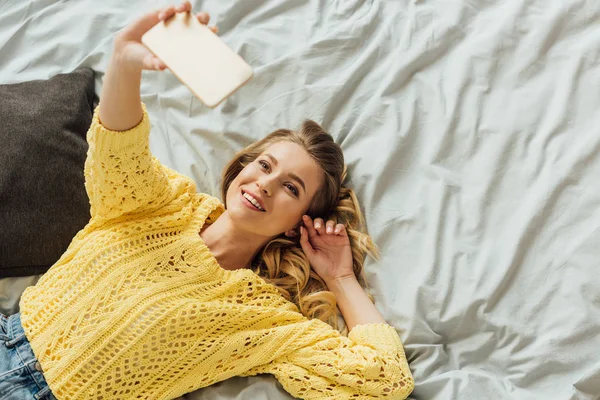 Blick von oben auf das schöne Mädchen, das im Bett liegt und ein Selfie auf dem Smartphone macht — Stockfoto