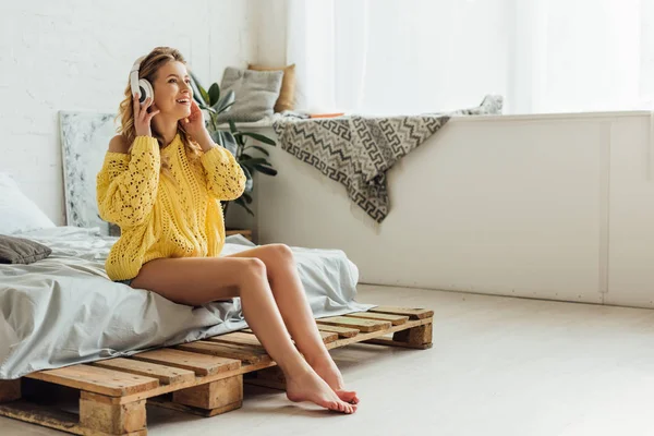 Schöne lächelnde junge Frau mit Kopfhörern, die auf dem Bett sitzt und zu Hause mit Kopierplatz Musik hört — Stockfoto