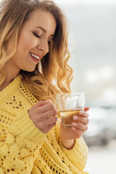 Вибірковий фокус красивої усміхненої молодої жінки, що тримає чашку чаю — стокове фото