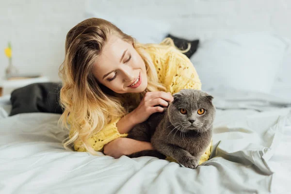 Bella ragazza in maglia maglione sdraiato a letto e abbracciando scozzese piega gatto — Foto stock