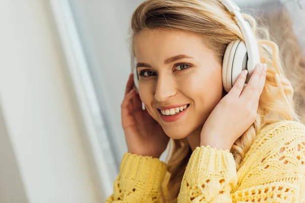 Schöne lächelnde junge Frau mit Kopfhörer, die in die Kamera schaut, während sie zu Hause Musik hört — Stockfoto