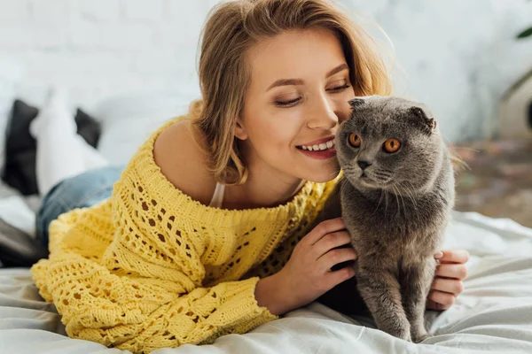 Bela menina sorridente em camisola de malha abraçando adorável escocês dobra gato em casa — Fotografia de Stock