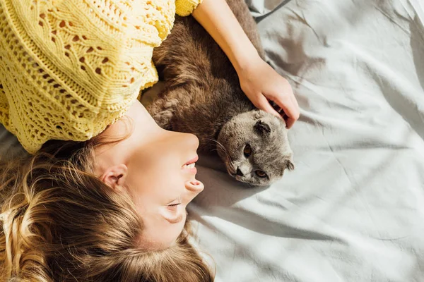 Vista superior de la hermosa mujer joven durmiendo en la cama con lindo gato pliegue escocés - foto de stock