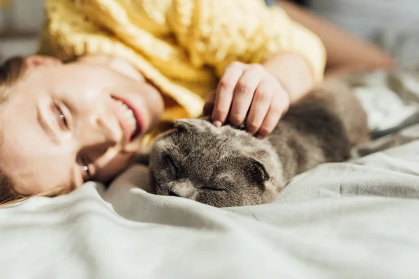 Selective focus of beautiful smiling girl stroking scottish fold cat at home — Stock Photo