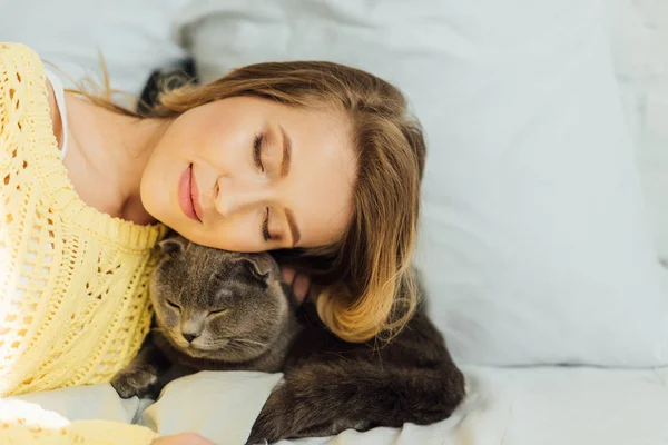 Belle jeune femme avec les yeux fermés couché dans le lit avec adorable chat écossais pliant — Photo de stock