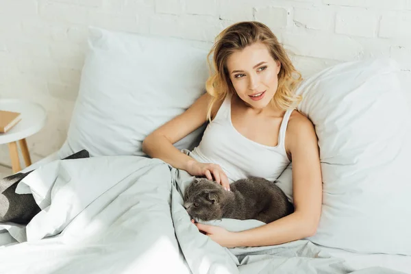 Beautiful girl lying in bed and hugging scottish fold cat with copy space — Stock Photo