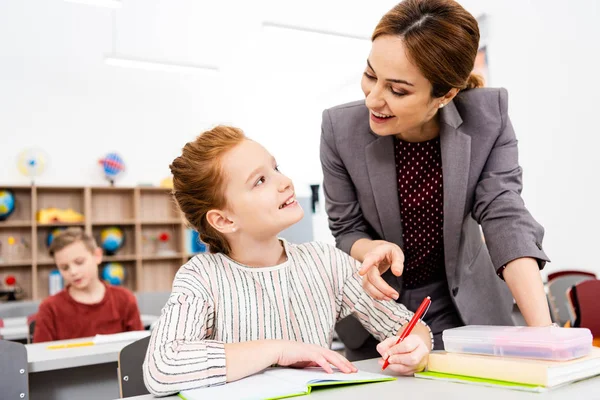 Teacher standing near desk and explaining lesson to pupil in classroom — Stock Photo