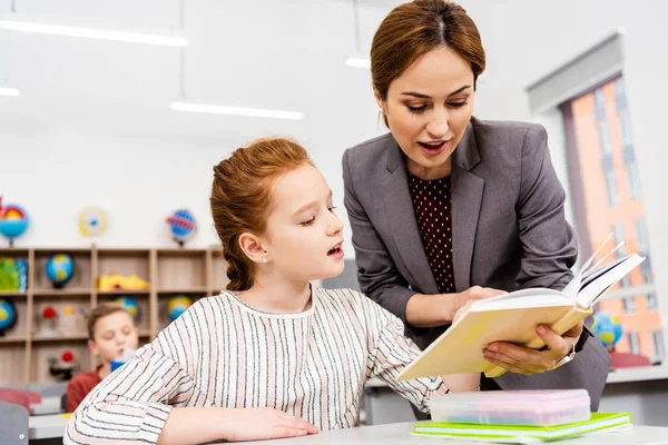 Teacher standing near desk and explaining lesson to pupil in classroom — Stock Photo