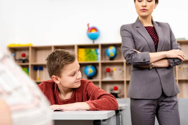 Cropped view of serious teacher in suit standing with crossed arms and looking at pupils — Stock Photo