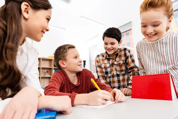 Lächelnde Schüler mit Notizbüchern und Büchern diskutieren im Klassenzimmer — Stockfoto