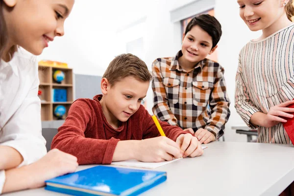Smiling pupils with notebooks and books discussing in classroom — Stock Photo