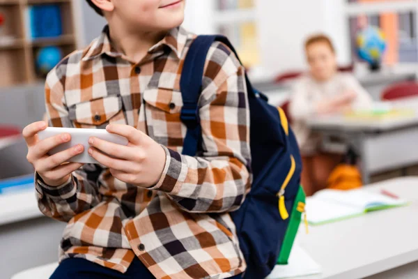 Vista parcial do aluno em camisa quadriculada com mochila usando smartphone em sala de aula — Fotografia de Stock