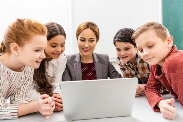 Smiling teacher and pupils using laptop during lesson in classroom — Stock Photo
