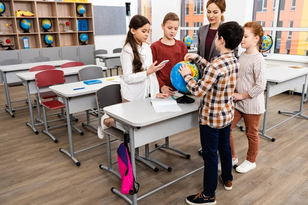 Profesores y alumnos mirando el globo mientras estudian geografía en el aula - foto de stock