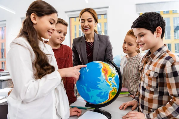 Вчитель і учні дивляться на земну кулю під час вивчення географії в класі — стокове фото