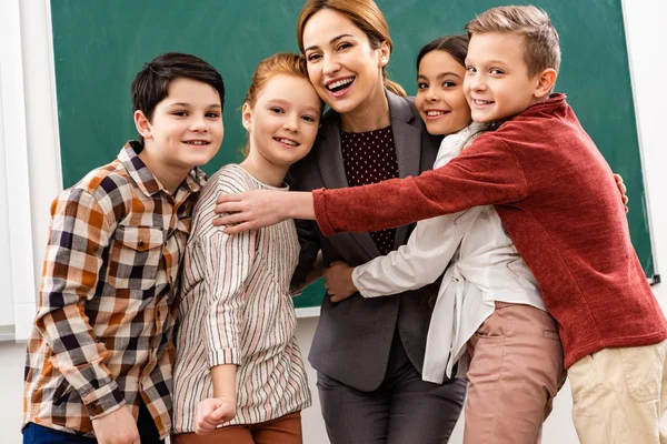 Щасливі учні обіймають вчителя перед дошкою в класі — стокове фото