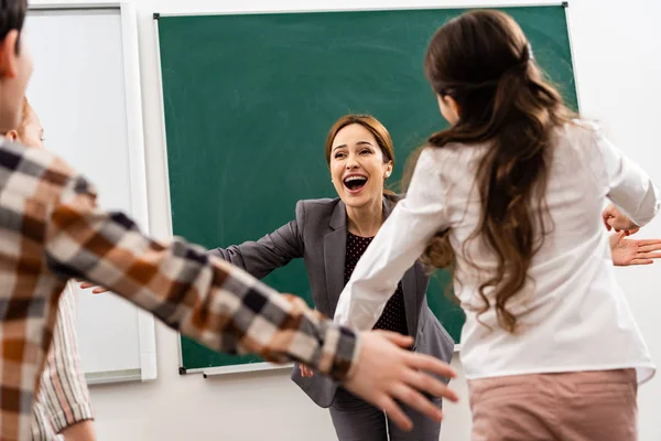 Happy pupils embracing teacher in front of blackboard in classroom — Stock Photo