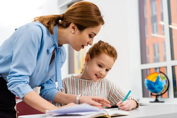 Teacher in blue blouse explaining lesson to pupil in classroom — Stock Photo