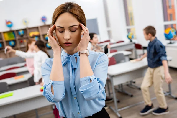 Professor cansado de blusa azul em pé na frente de mesas e rosto comovente — Fotografia de Stock