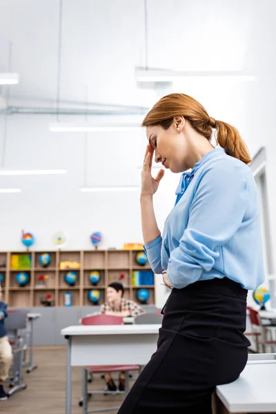 Professor cansado em blusa azul em pé perto da mesa em sala de aula — Fotografia de Stock