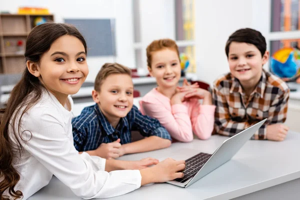 Happy preteen pupils using laptop in classroom with smile — Stock Photo