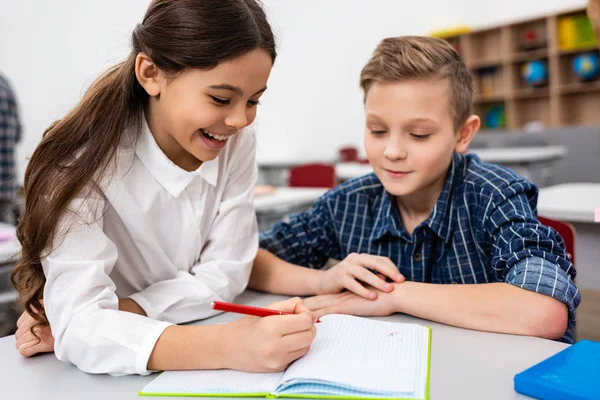 Dois alunos escrevendo em caderno na mesa em sala de aula — Fotografia de Stock