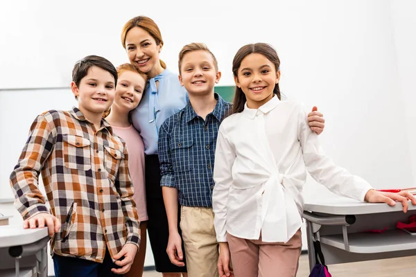 Lachender Lehrer mit Schülern, die im Klassenzimmer stehen und in die Kamera schauen — Stockfoto