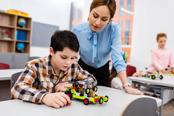 Insegnante in camicetta blu guardando pupilla con giocattolo educativo — Foto stock