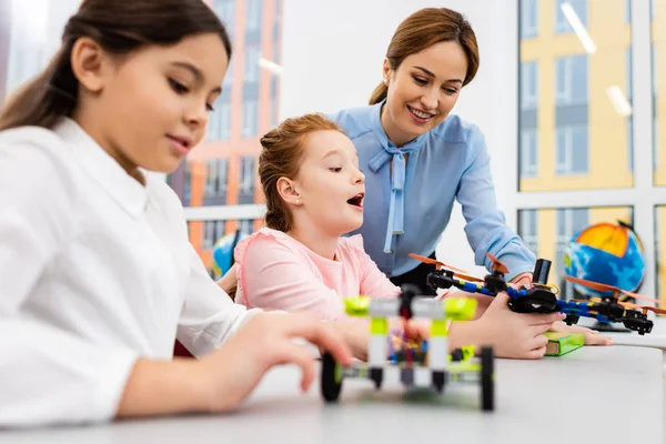 Profesor sonriente de pie cerca de los alumnos con juguetes educativos en el aula - foto de stock